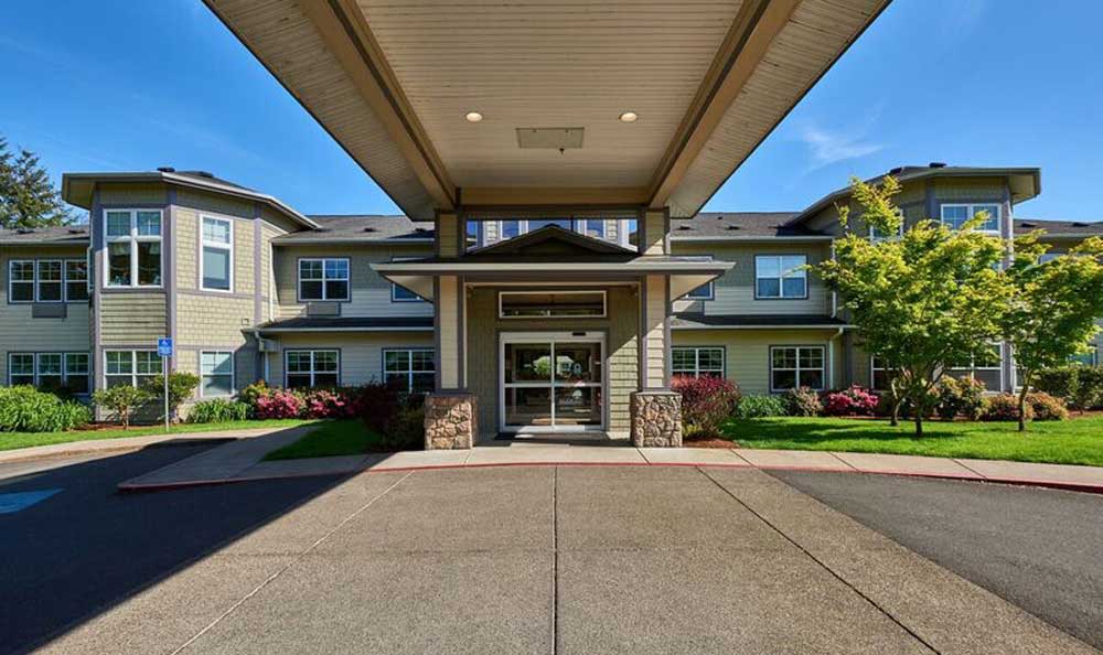 A modern building entrance with a covered driveway and landscaped surroundings.
