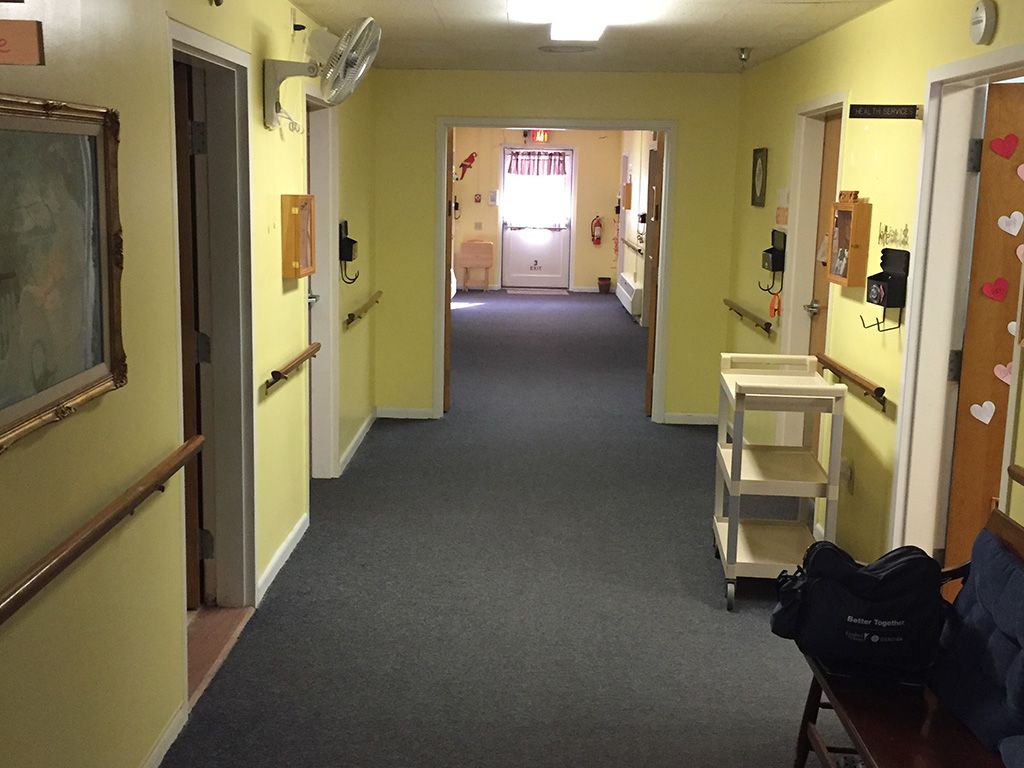 A hallway in a building with yellow walls, carpeted floor, handrails, and multiple doors.