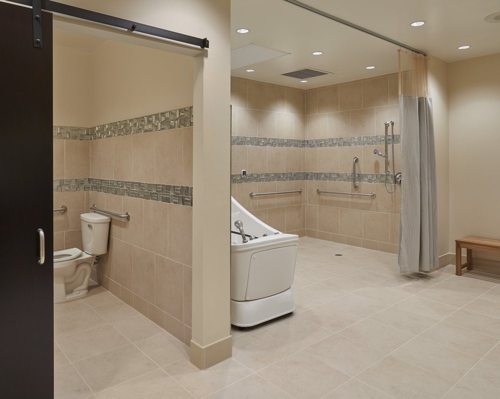 A spacious and accessible bathroom with a walk-in tub, toilet, and handrails for support.