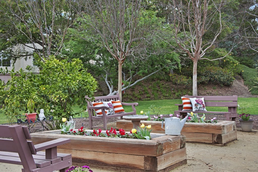 A serene garden area with wooden planters, colorful cushions, and lush greenery.