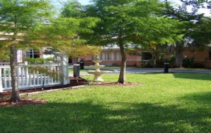 A tranquil garden scene with a tree, fountain, and well-maintained grass.