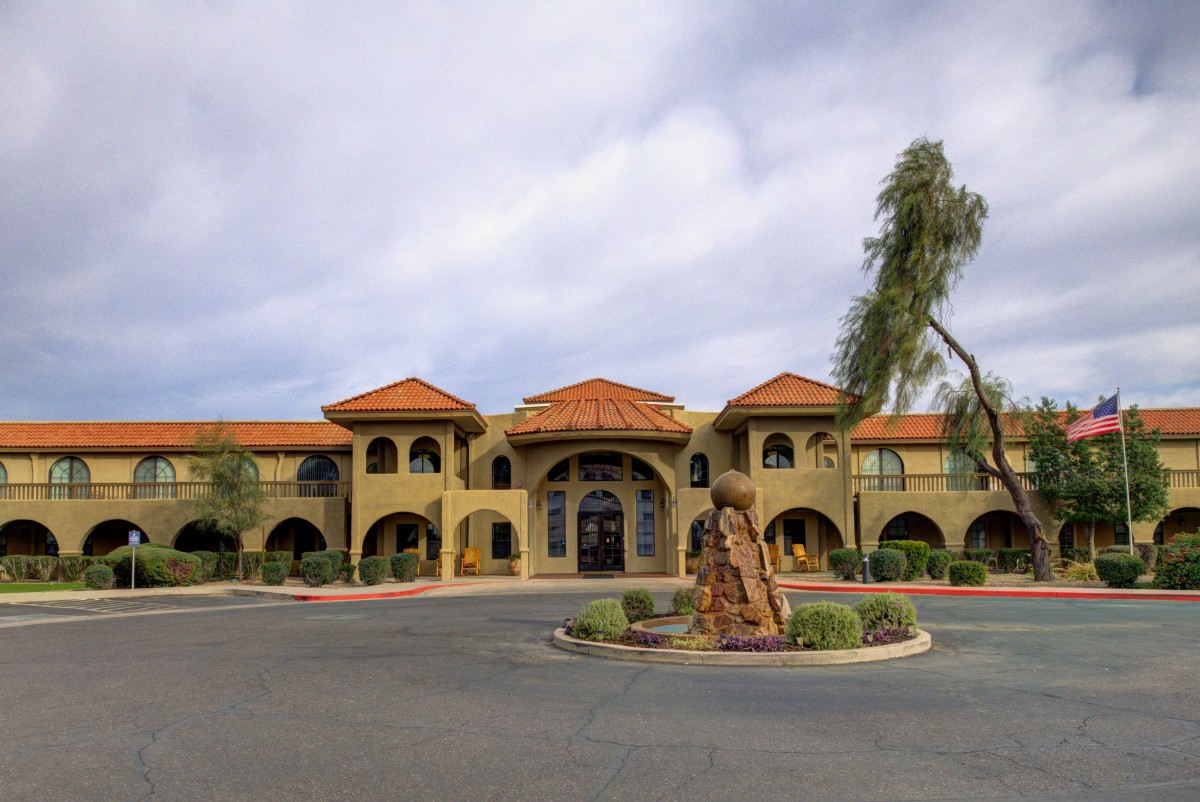 A Spanish-style building with a terracotta roof, framed by palm trees and a central statue at the entrance.