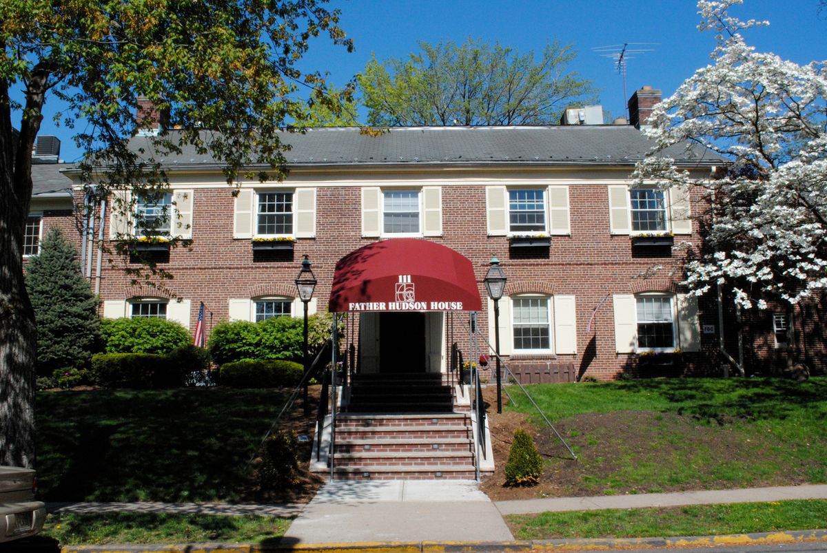 A brick building with a red awning covering the entrance, surrounded by greenery.