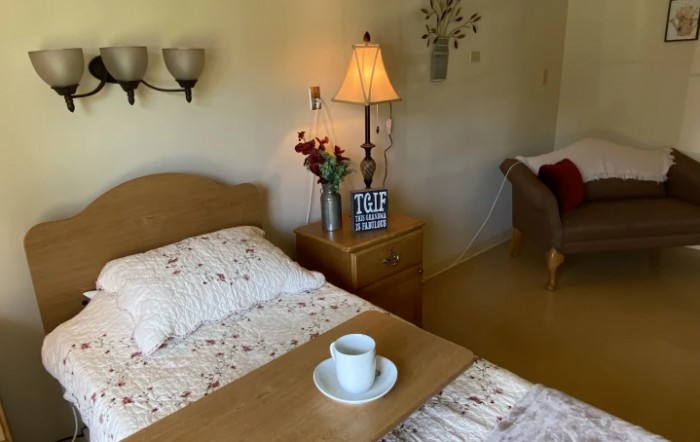 A cozy bedroom with a neatly made bed, a nightstand holding a lamp, vase of flowers, and a teacup.