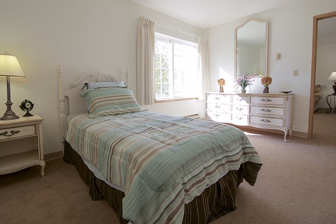 A cozy bedroom featuring a single bed with striped bedding, a dresser with a mirror, and large window with curtains.