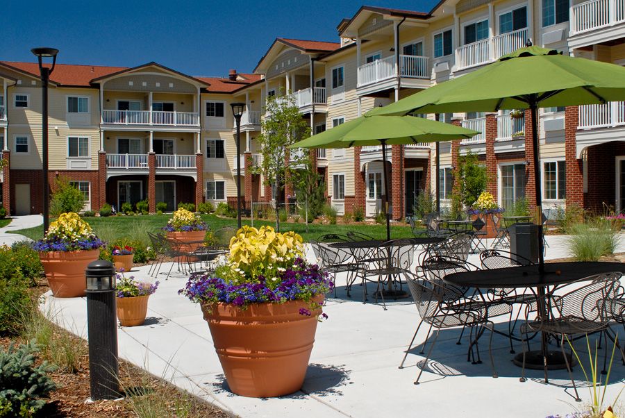 A sunny courtyard with outdoor seating and vibrant flowers in front of a modern residential building.