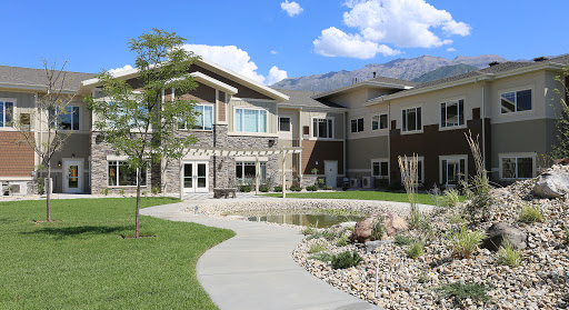 A modern residential building surrounded by landscaped grounds and a serene pond.