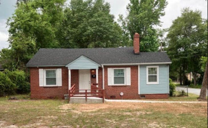 A single-story brick house with a blue accent and a spacious front yard.