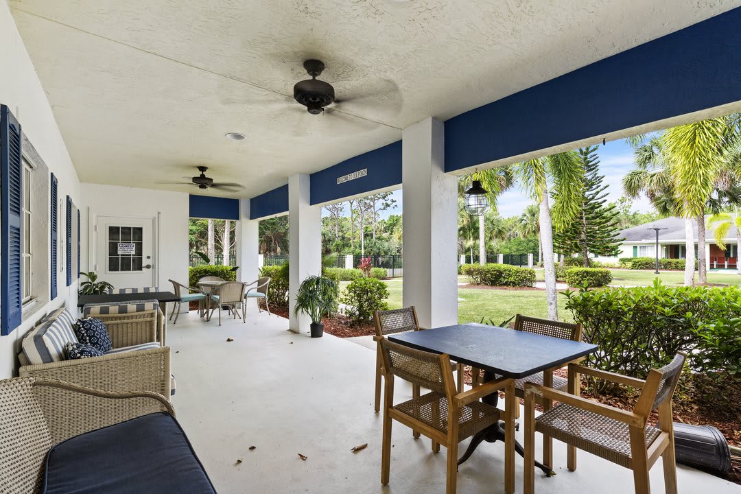 A spacious covered patio with tables and chairs, enhanced by ceiling fans and overlooking a lush garden.