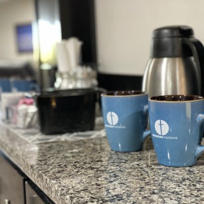 A countertop with two blue mugs and a coffee pot in a kitchen setting.