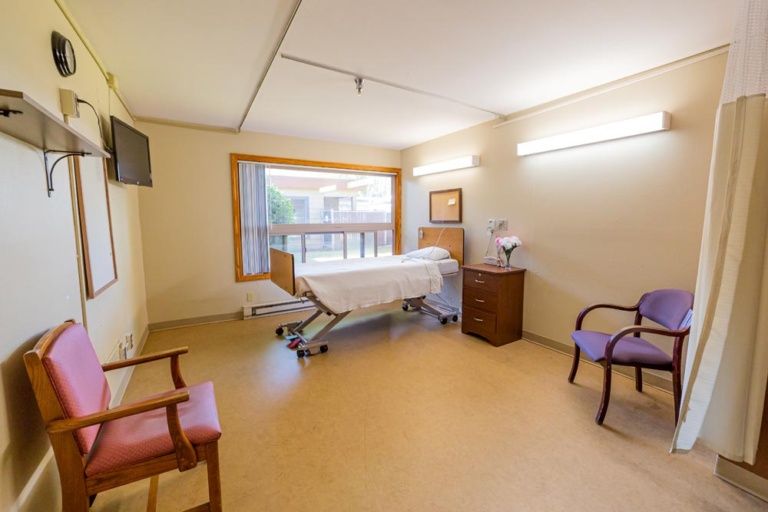 A clean and well-lit hospital room with a patient bed, chairs, and medical equipment.