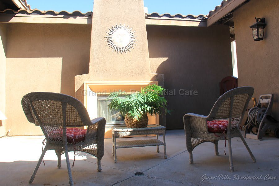 A cozy patio with wicker chairs and a fireplace, enhanced by sunlight and greenery.