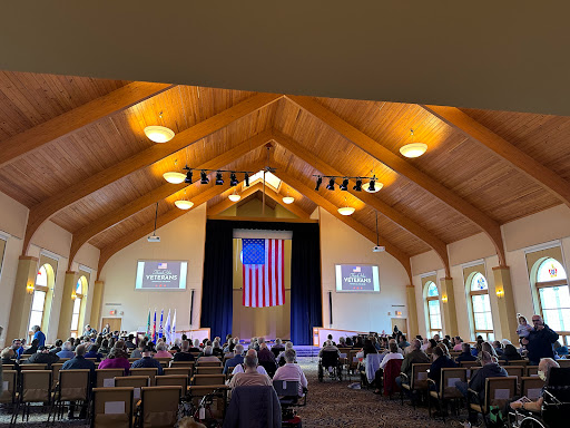 A congregational gathering in a beautifully designed wooden church interior, featuring an American flag as the focal point.