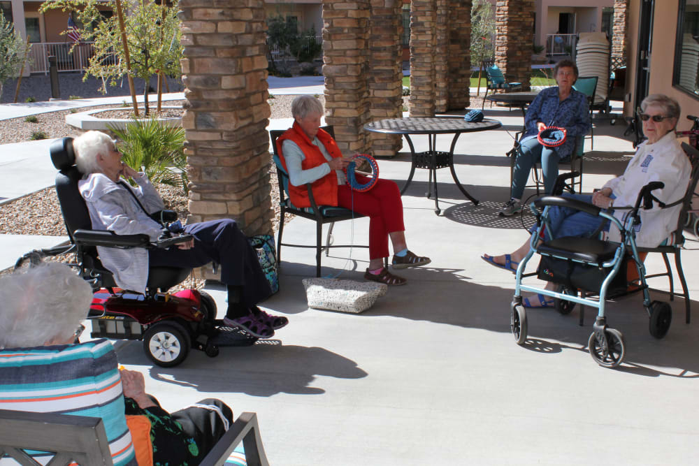 A group of seniors socializing outdoors on a sunny patio, with some using wheelchairs.