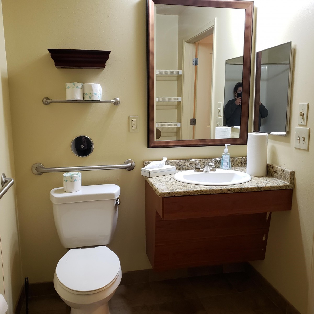 A clean and tidy bathroom with a sink, mirror, toilet, and shelves with towels.