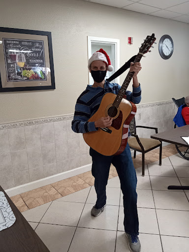 A cheerful musician dressed for the holidays poses with a guitar, ready to entertain.