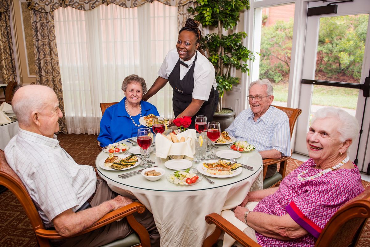 A group of seniors enjoying a meal together at a restaurant served by an attentive waiter.