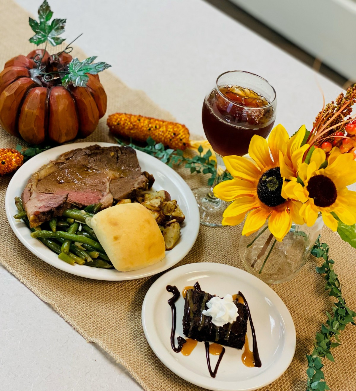 A festive Thanksgiving meal with roast beef, green beans, and a roll, accompanied by a decadent brownie dessert and autumnal decorations.
