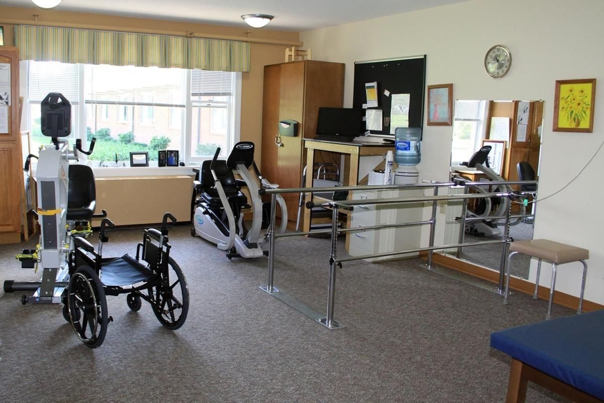 A physical therapy room equipped with exercise machines, a wheelchair, and parallel bars.