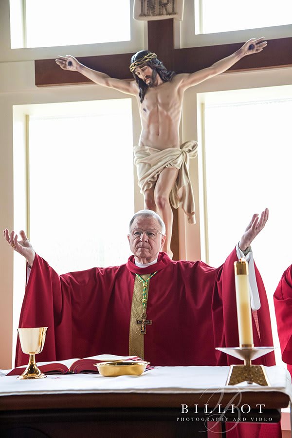 A priest in red vestments conducting a religious service at the altar with a crucifix behind him.