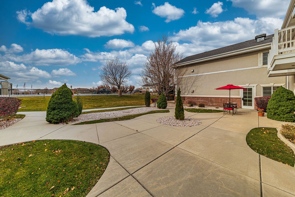 A peaceful outdoor patio area with a red umbrella and landscaped pathway beside a building under a partly cloudy sky.