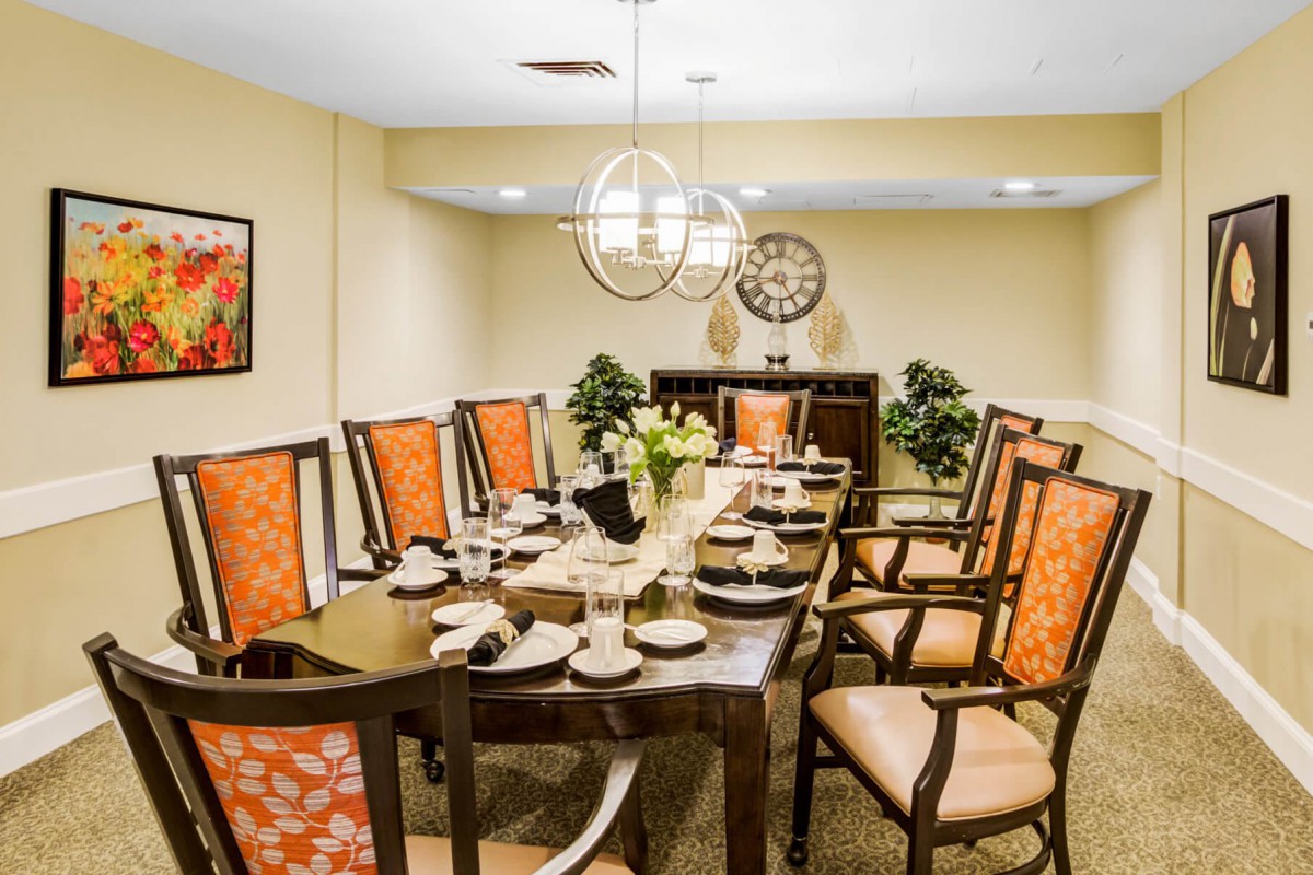 A well-decorated dining room with a large table set for a meal, featuring elegant chairs, modern lighting fixtures, and decorative elements.