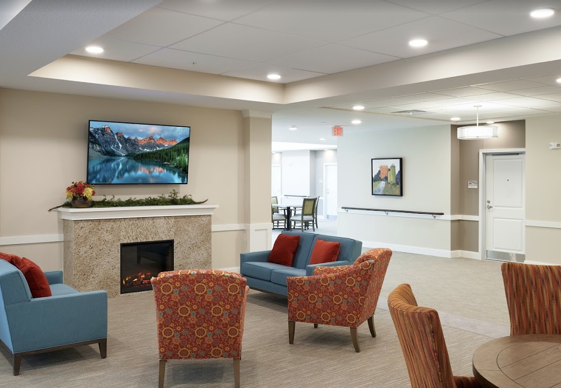 A modern living room with a cozy seating area, featuring a television above the fireplace and stylish armchairs.