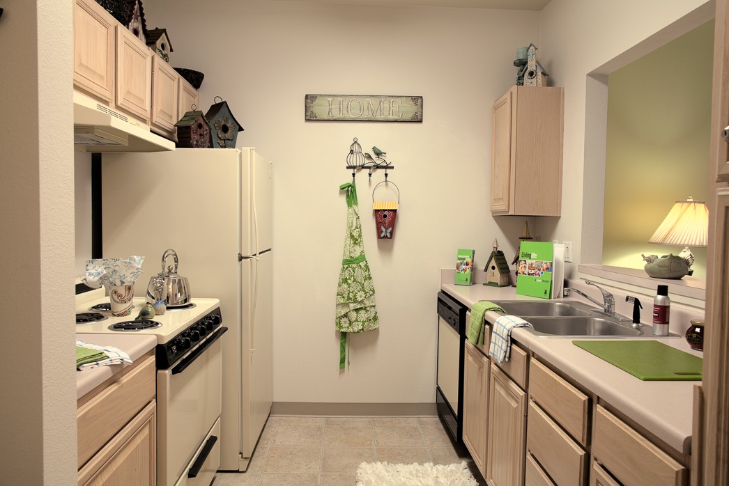 A cozy kitchen with light wooden cabinets, decorated with green accents and a neatly hung apron.