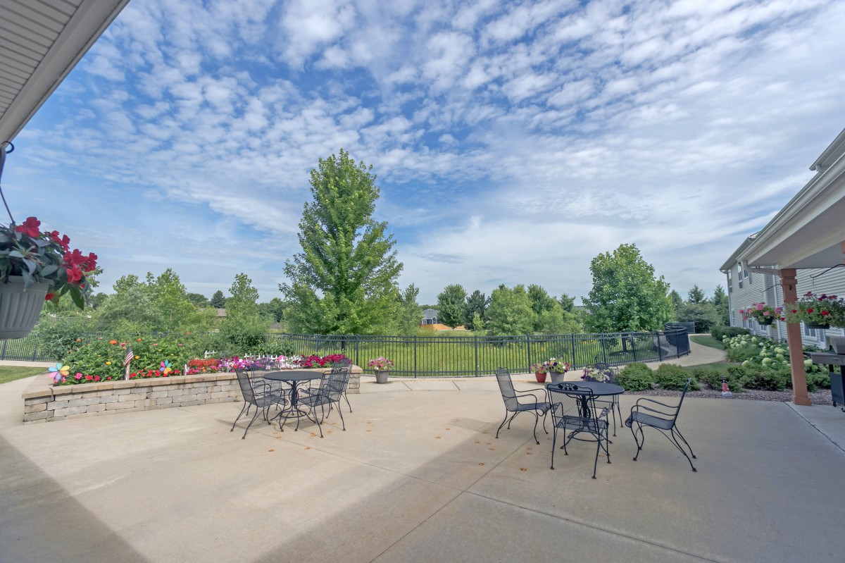 A spacious outdoor patio with tables and chairs, surrounded by lush greenery and a partly cloudy sky.