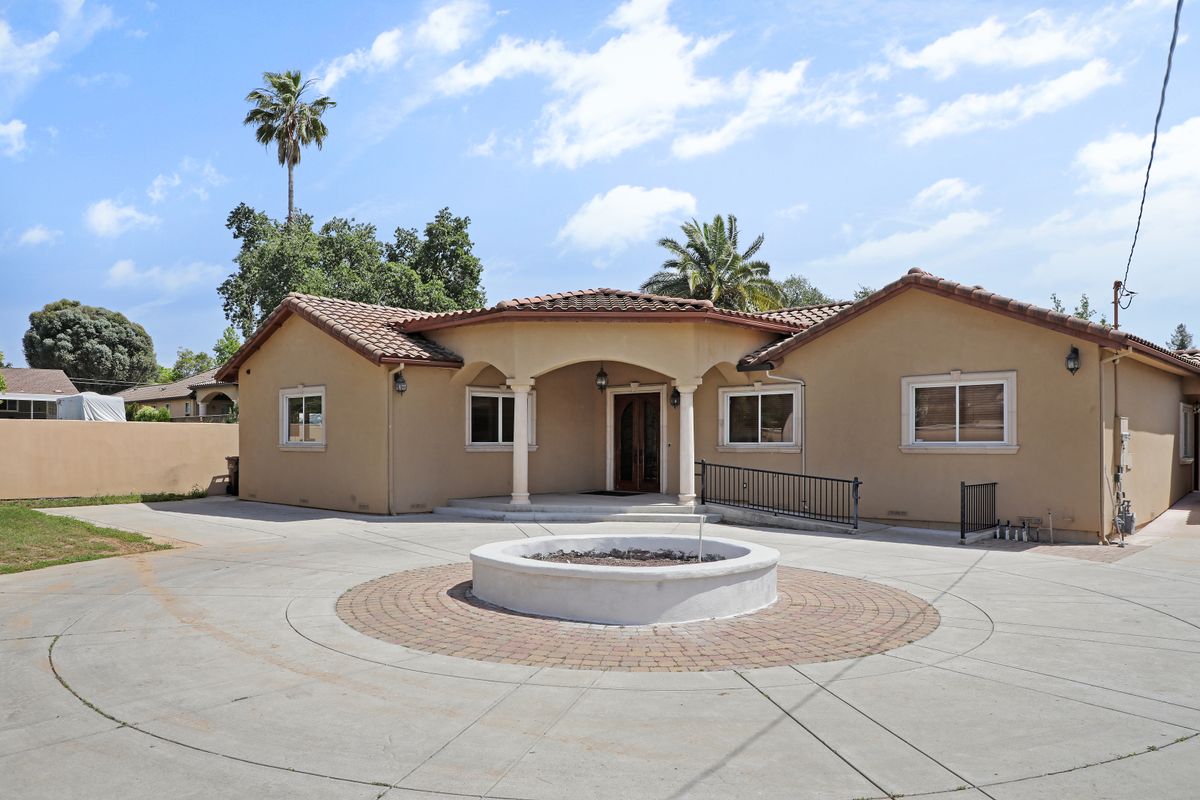 A beige residential house with a fountain in the front yard and palm trees surrounding the property.