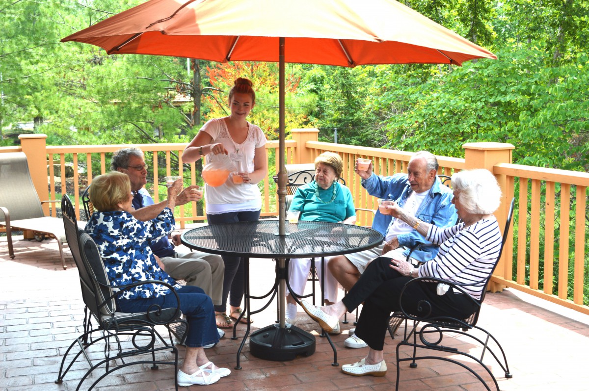 A group of people sitting around a table with an umbrella, enjoying a conversation outdoors on a deck.