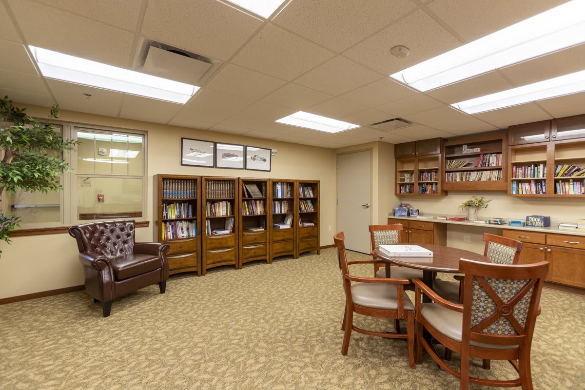 A cozy library setting with bookshelves, a table, and chairs under fluorescent lighting.