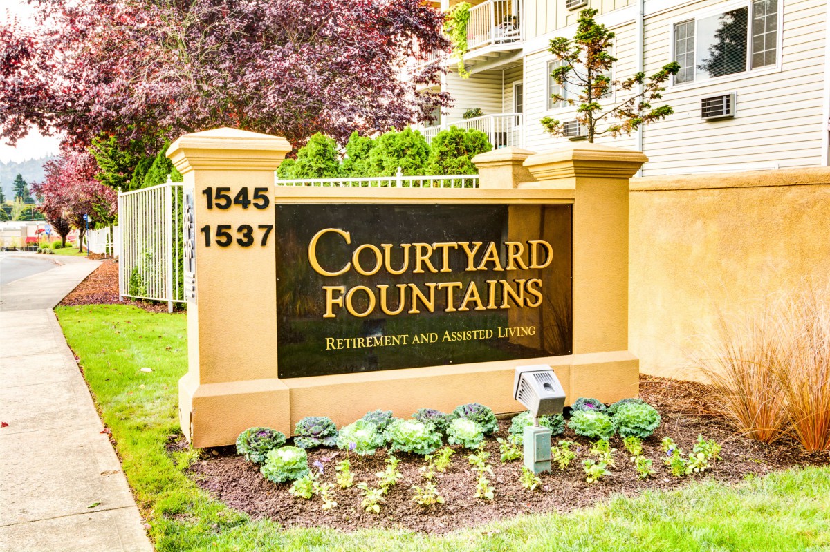 Entrance sign for Courtyard Fountains apartment complex with landscaped surroundings.