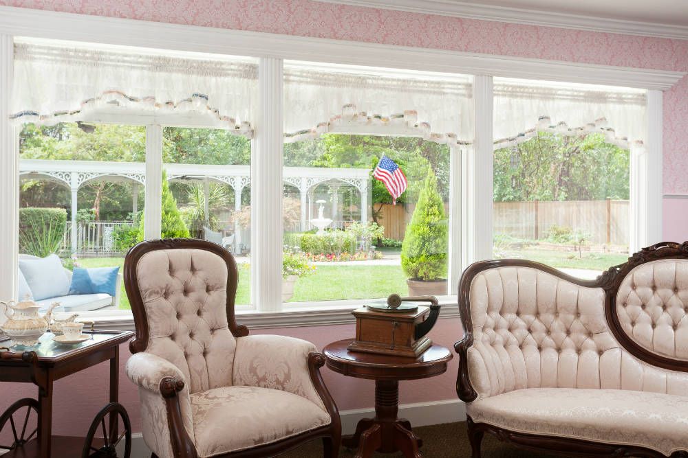 A cozy sitting area with antique chairs overlooking a garden through large windows.