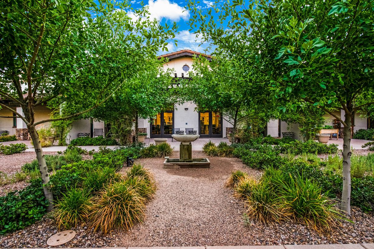 A serene courtyard garden with a central fountain, flanked by lush greenery and a charming building in the background.