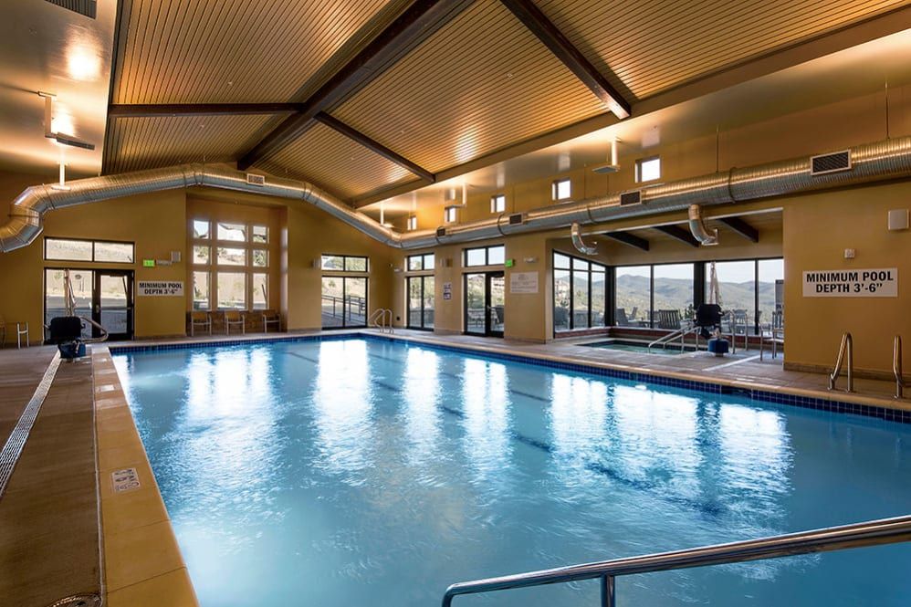An inviting indoor swimming pool with large windows and a wooden ceiling.