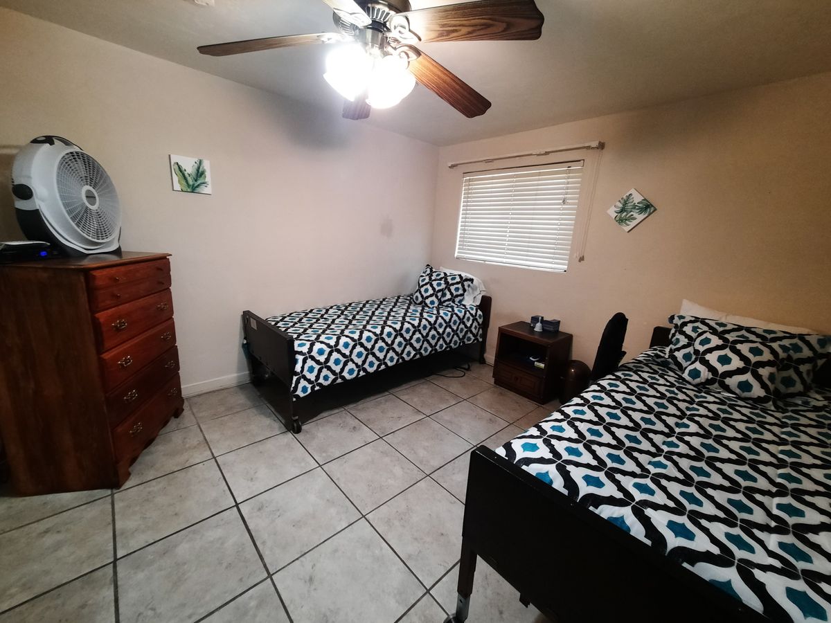 A tidy bedroom featuring twin beds with geometric-patterned bedding, a ceiling fan, and tiled flooring.