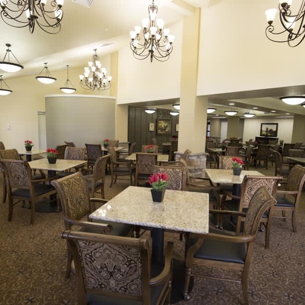 An elegant dining room with multiple tables and chairs, illuminated by chandeliers.