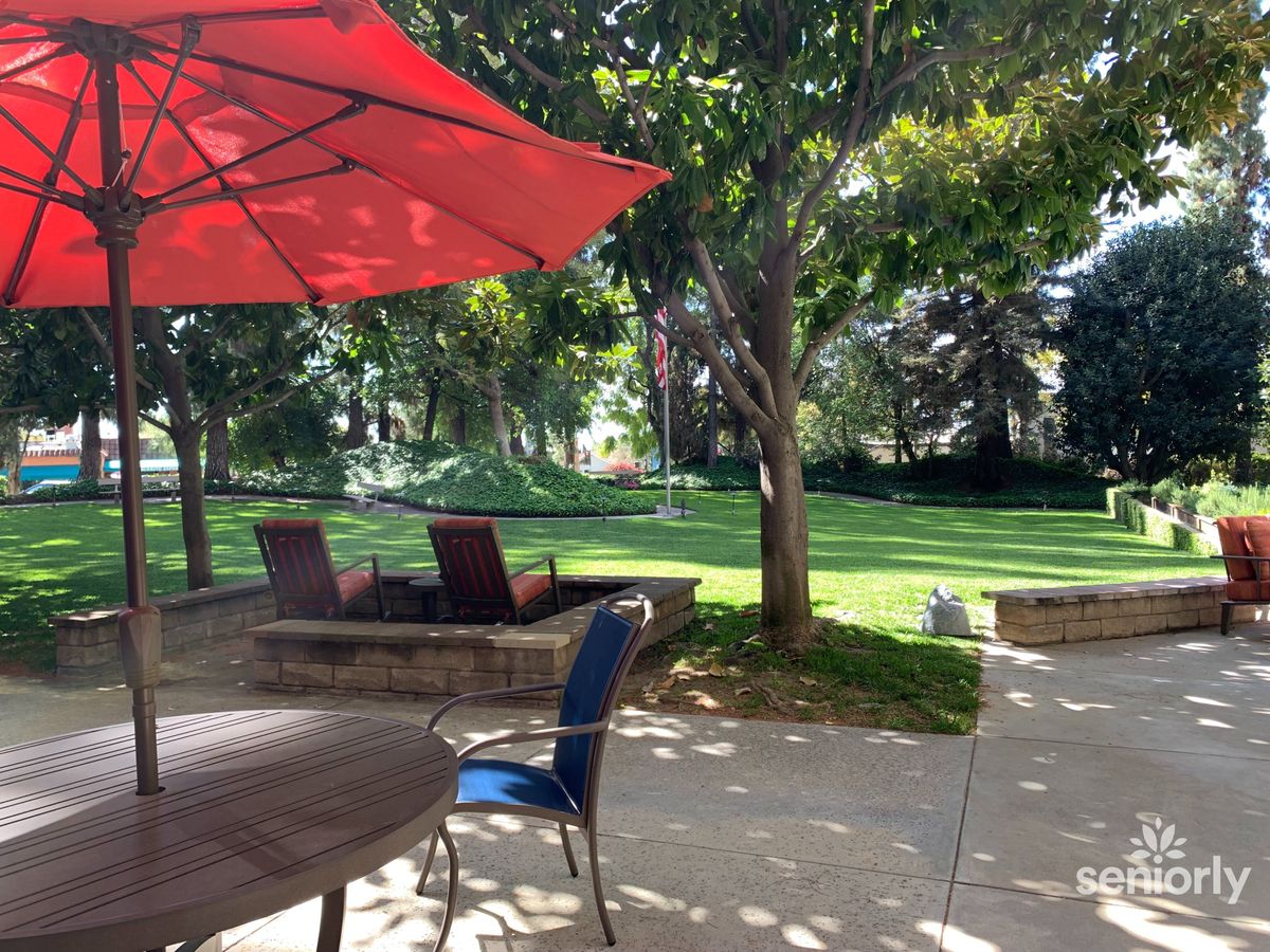 A tranquil outdoor patio area with tables, chairs, and a vibrant red umbrella overlooking a lush garden.