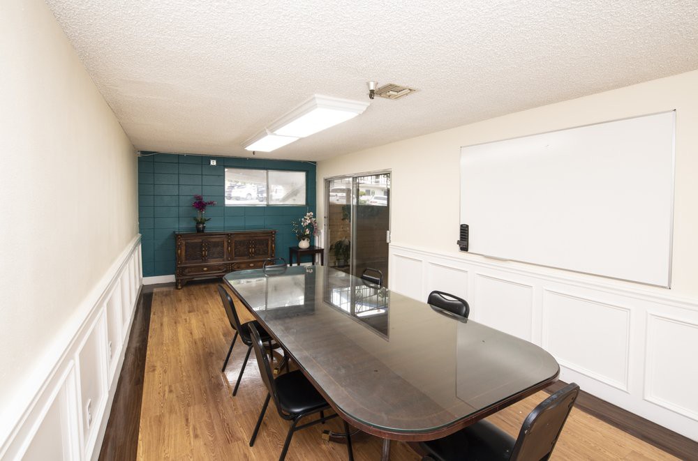 A modern meeting room with a long conference table and chairs, featuring wooden flooring and a decorative wall.