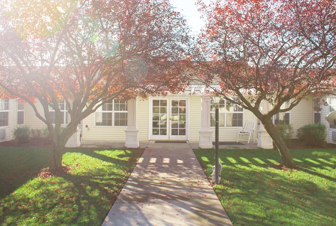A sunny day view of a house with mature trees and a pathway leading to the entrance.