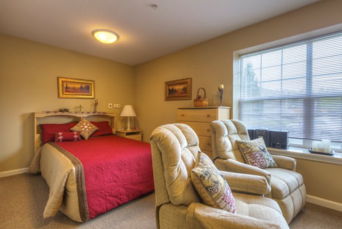 A cozy bedroom featuring a red bedspread, two comfortable chairs, and decorative elements.