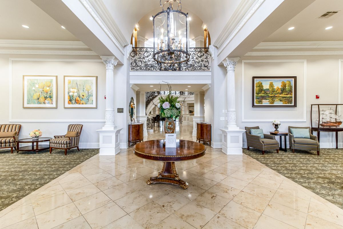 A luxurious lobby with elegant furnishings, a central table adorned with flowers, and a large chandelier overhead.