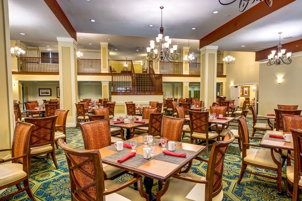 A spacious and elegantly designed dining area with neatly arranged tables and chairs, illuminated by chandeliers.