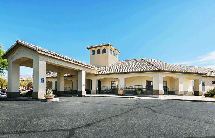 A hotel building with a tiled roof and parking area under a clear blue sky.