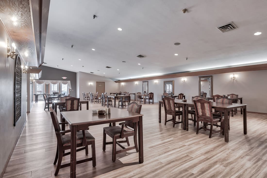 A spacious dining area with wooden tables and chairs arranged on a light wood floor.