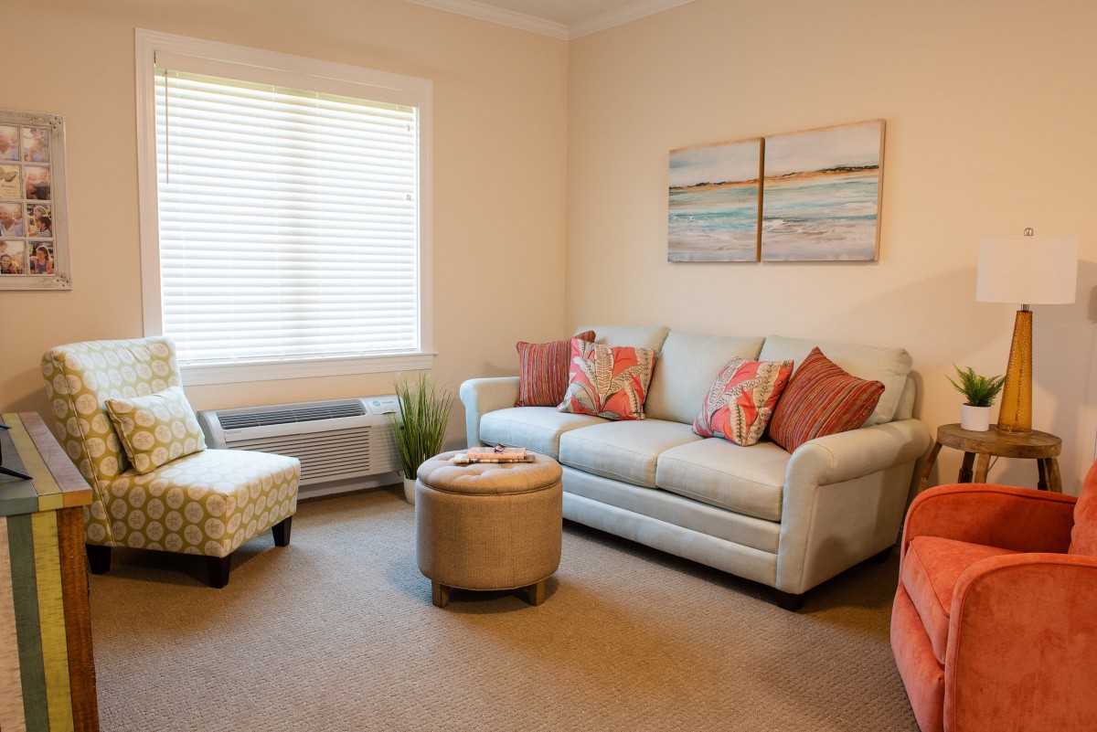 A cozy living room with a sofa, cushions, an armchair, and artwork on the wall.