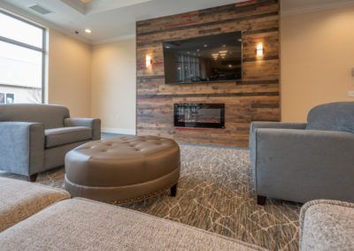 A modern living room with a cozy seating area, featuring a large TV and a fireplace set in wood paneling.