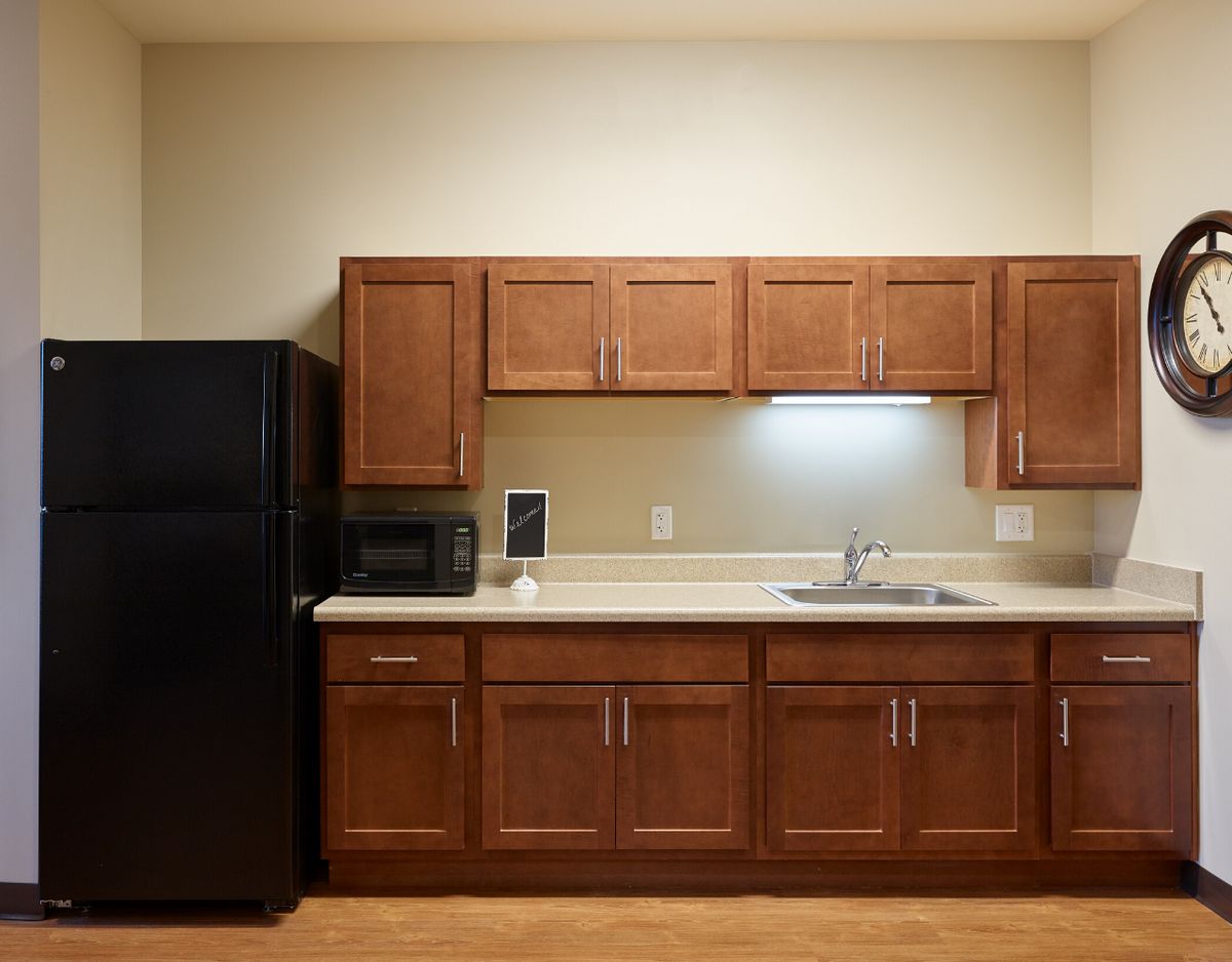 A kitchen with wooden cabinets, a black refrigerator, a microwave, and a sink.
