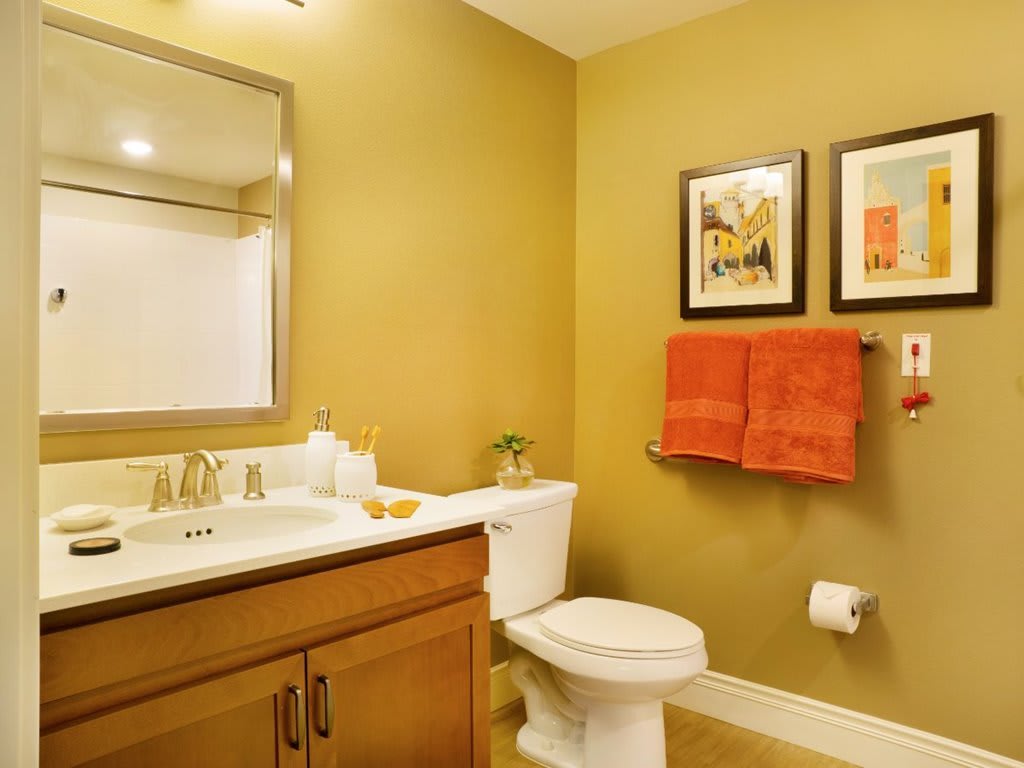A well-designed bathroom with a sink, mirror, and toilet, featuring warm yellow walls and red towels.